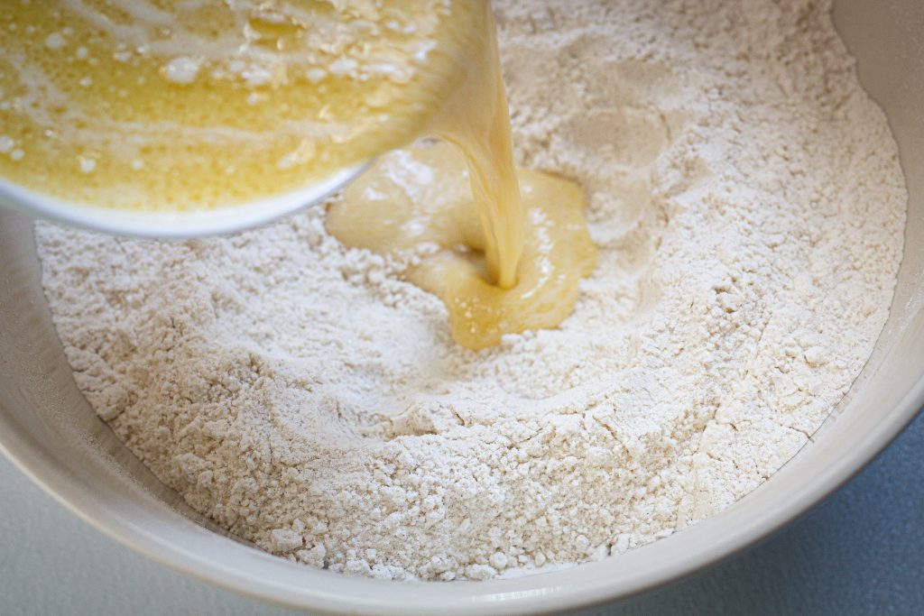 Wet ingredients being poured into a well made in the dry ingredients for a muffin recipe