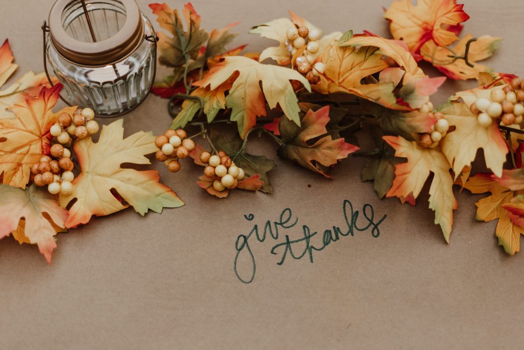 decorative Fall leaves and a glass lantern above the handwritten cursive words "give thanks" written on kraft paper